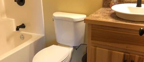 Un baño con inodoro blanco, bañera, lavamanos con espejo y armarios de madera.