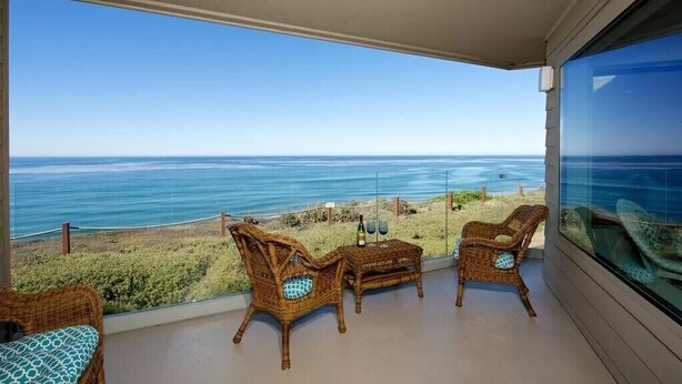 A balcony with wicker furniture overlooking a beach and ocean.