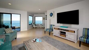 A spacious living room with a large TV, comfortable seating, and a view of the ocean.
