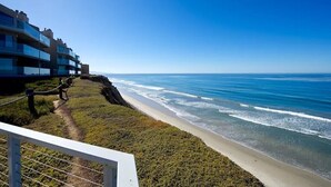 A coastal view with a beach, ocean, and a building with balconies overlooking the sea.