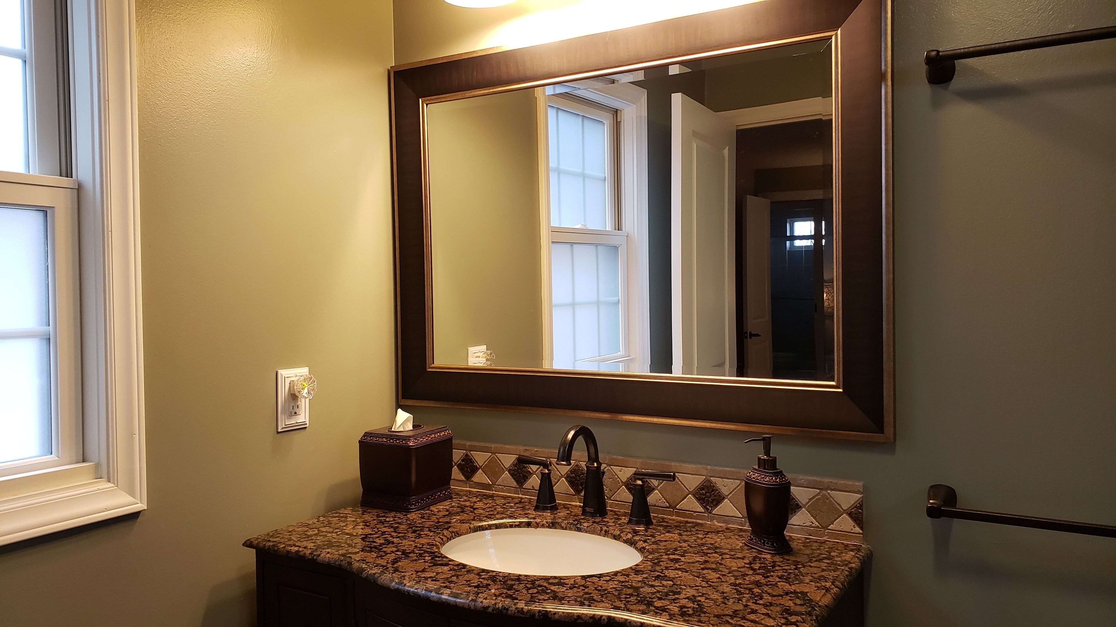 A bathroom with a granite countertop sink, a mirror, and a towel dispenser.