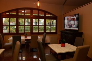 A restaurant with a large arched window, multiple tables, chairs, and a television on the wall. - Hotel Erbaluce (Caluso)