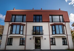 Un edificio de dos pisos con techo de tejas rojas, ventanas amplias y una entrada central.