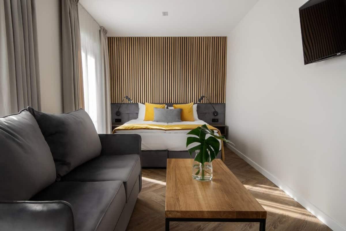 Une chambre d’hôtel moderne avec un lit, un canapé, une table basse en bois et une plante.