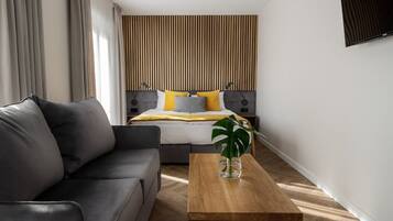 A modern hotel room with a bed, a sofa, a wooden coffee table, and a plant.