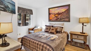 Une chambre à coucher avec un grand lit, une fenêtre avec des rideaux, un tableau accroché au mur et une table de chevet avec une lampe.