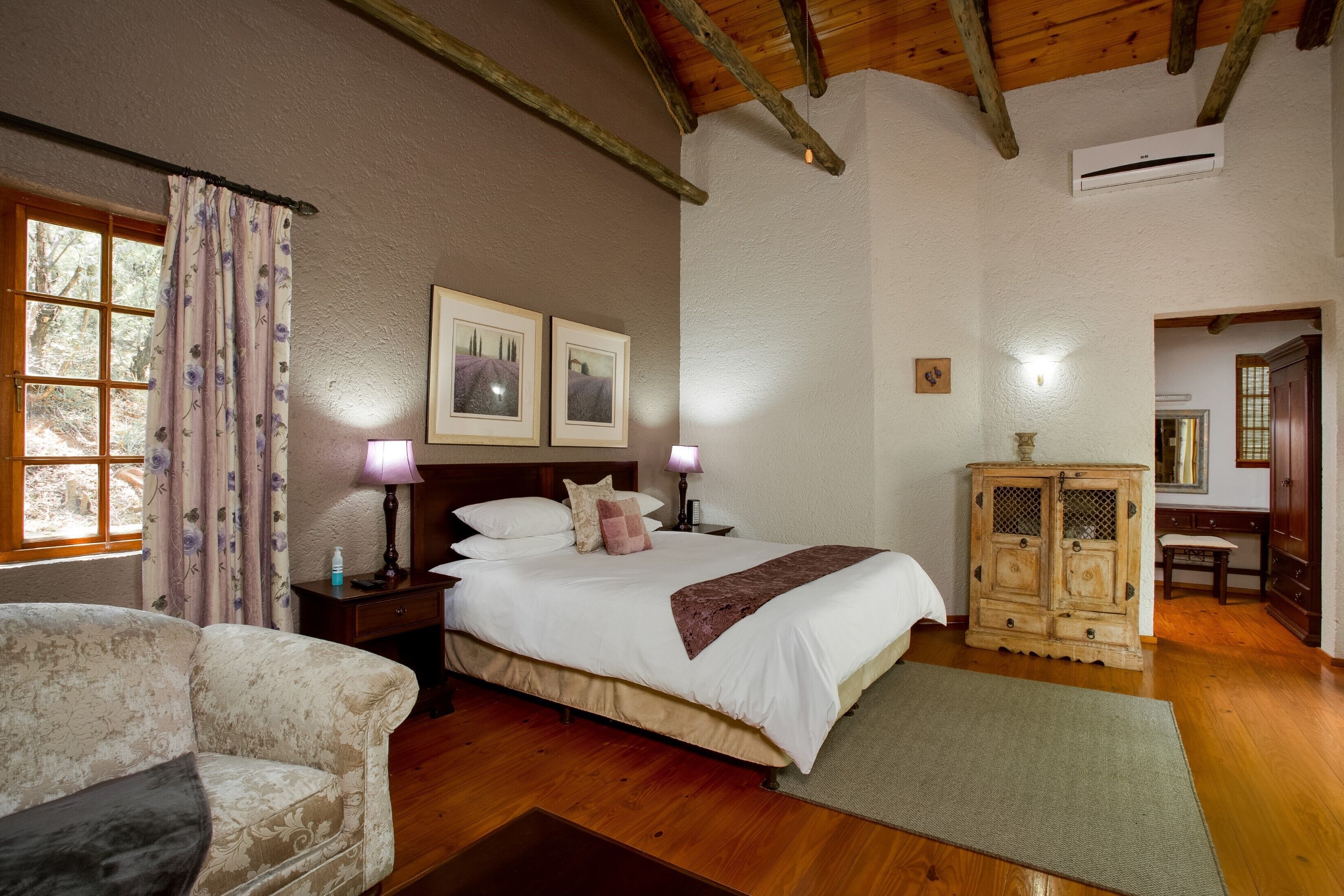 Een slaapkamer met een groot bed, houten vloer, een houten kast en een raam met gordijnen.