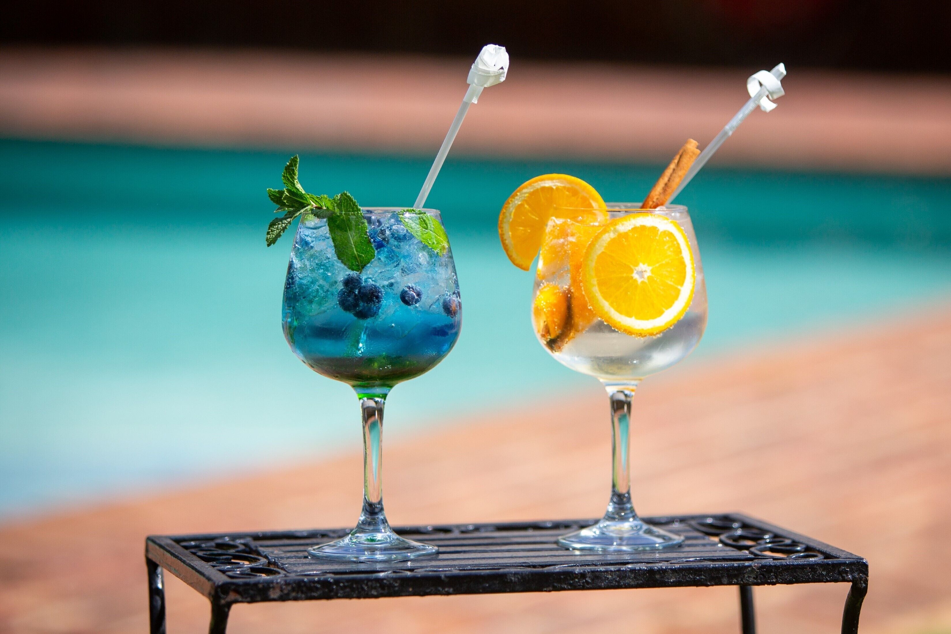 Two cocktails on a table by a poolside.