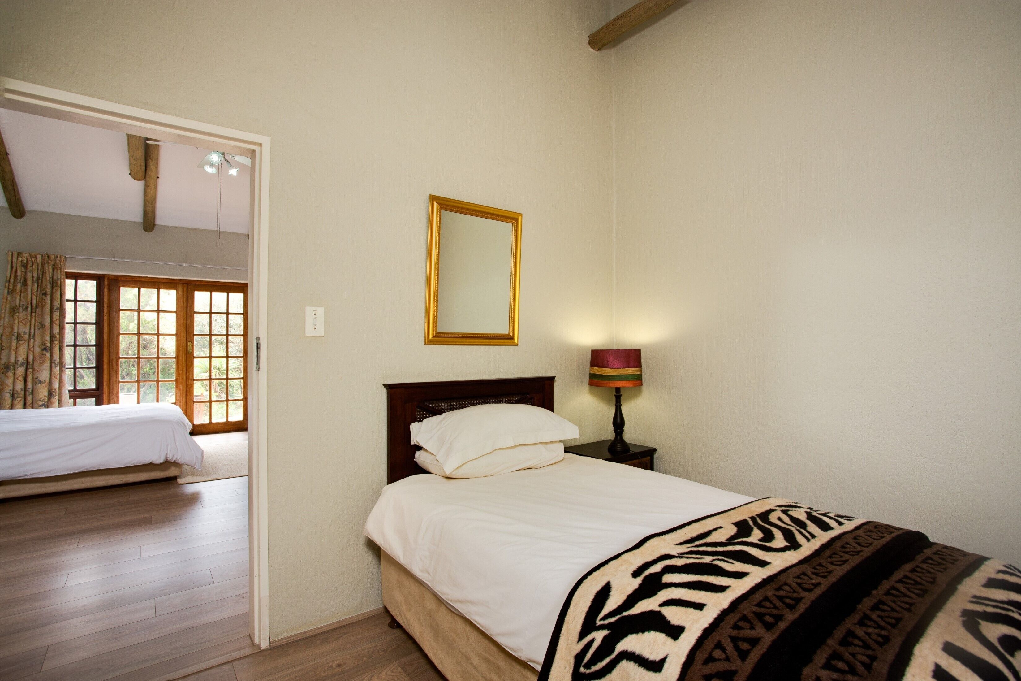 A bedroom with a bed, a nightstand with a lamp, a mirror on the wall, and a window with curtains.