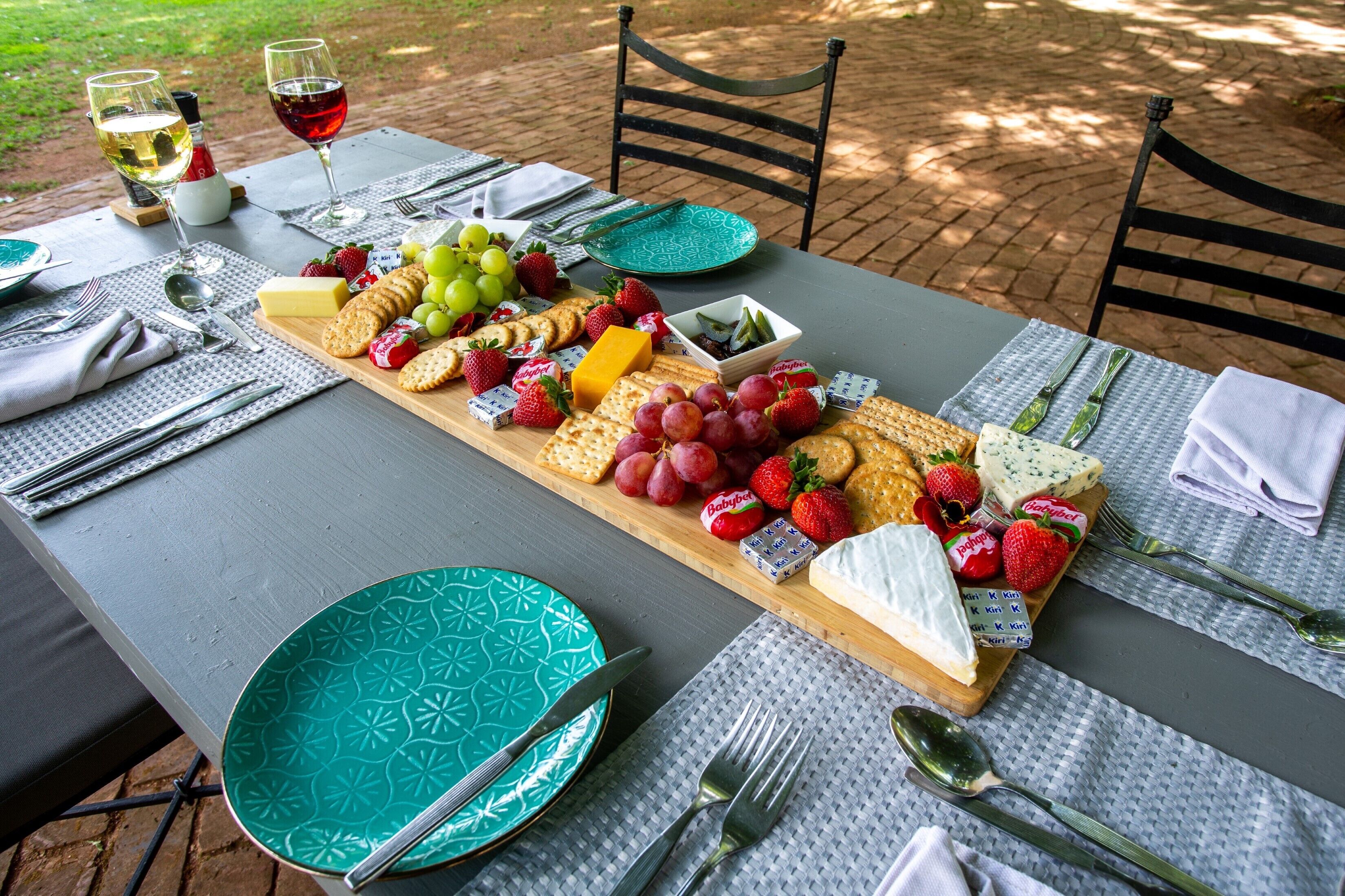 Une table dressée pour un repas, avec une planche de fromages, des fruits et des verres à vin.