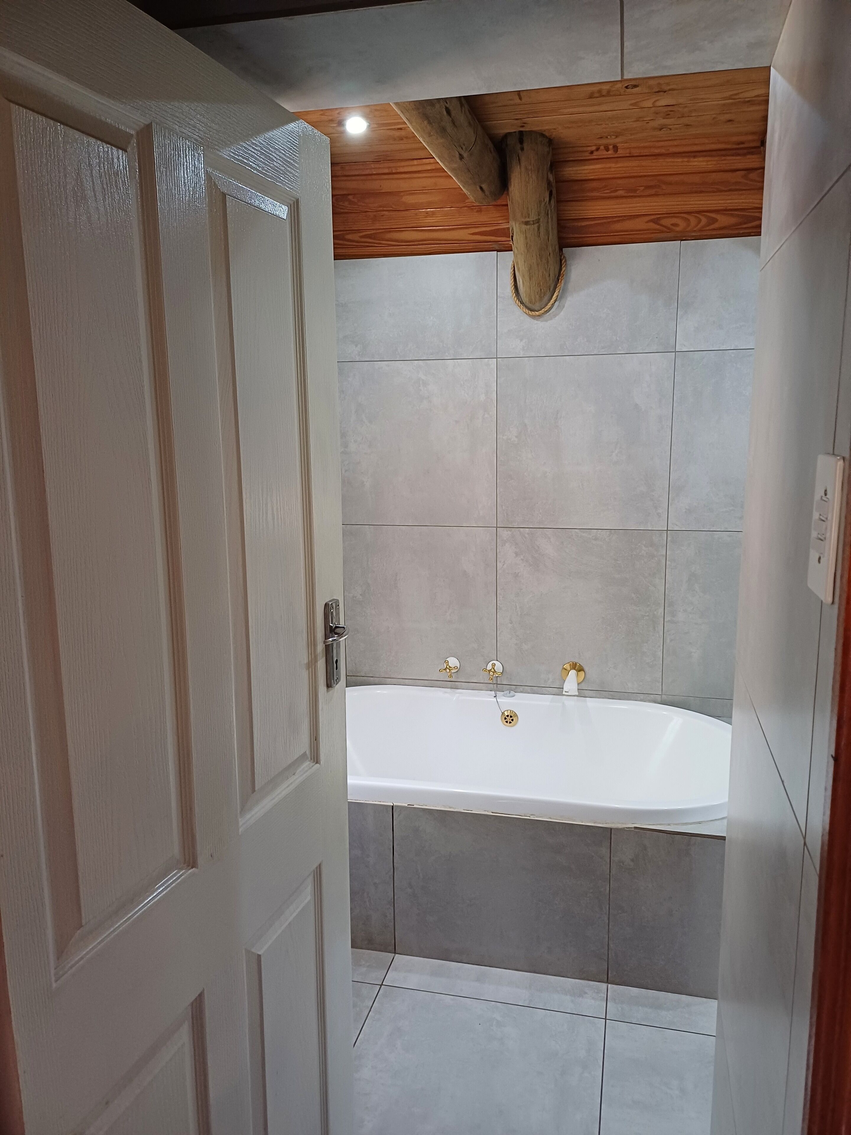 Un baño con bañera, vigas de madera en el techo y paredes de azulejos.