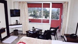 Habitación de hotel con cama, escritorio, silla, televisor, ventana que ofrece vistas a un templo y árboles, y teléfono sobre una mesita de noche.