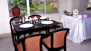 Un comedor con una mesa dispuesta para dos, sillas, un ventanal con vistas a la vegetación y una mesa con utensilios de cocina.