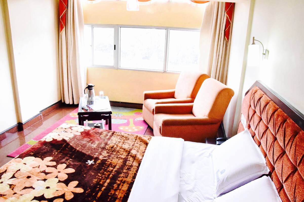 Een hotelkamer met een bed, twee fauteuils, een salontafel, een raam en een kleurrijk vloerkleed.