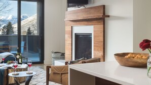 Una sala de estar moderna con chimenea, televisor montado encima y un ventanal con vistas a la montaña.