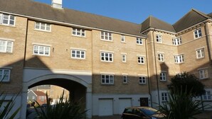 A multi-story brick building with a central archway, a car parked in front, and a swimming pool in the foreground. - Beachside Apartment (Eastbourne)