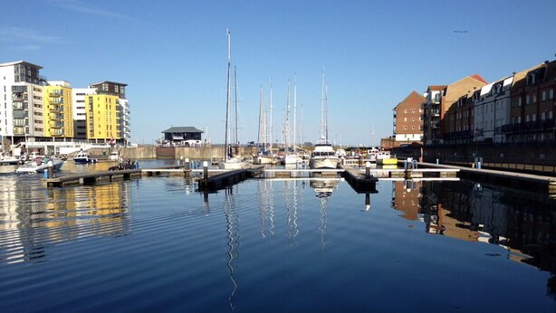 A marina with boats docked, buildings along the waterfront, and a clear sky. - Beachside Apartment (Eastbourne)