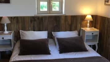 En dubbelsäng med två kuddar, ett sängbord med en lampa, en sänggavel i trä och ett fönster med utsikt över grönområden.