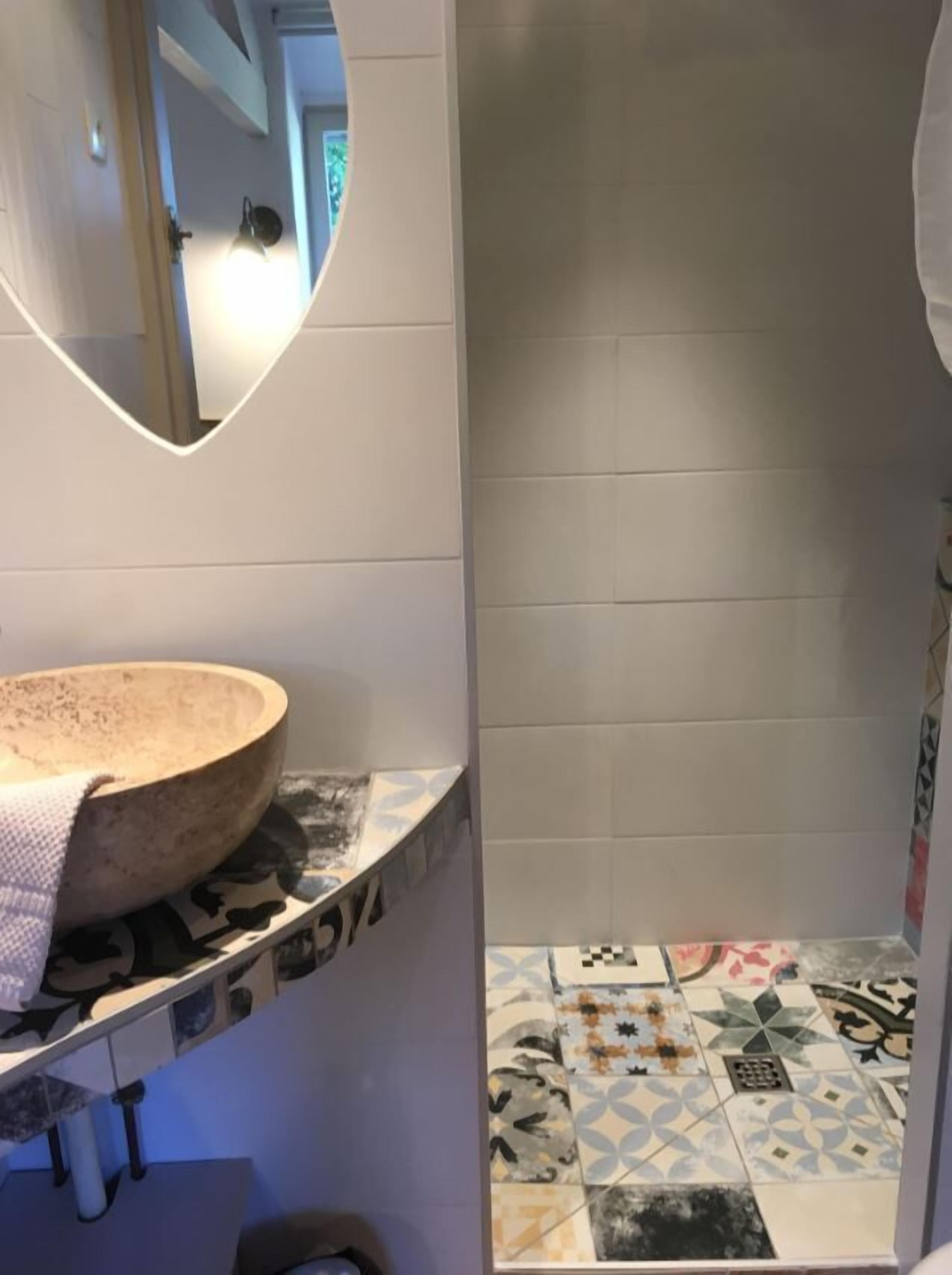 Un baño con un lavamanos redondo, un espejo y azulejos estampados.