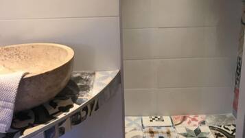 Un baño con un lavamanos redondo, un espejo y azulejos estampados.