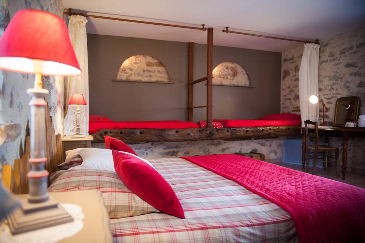 Un dormitorio rústico con una cama de madera, un edredón rojo y una mesita de noche con una lámpara.