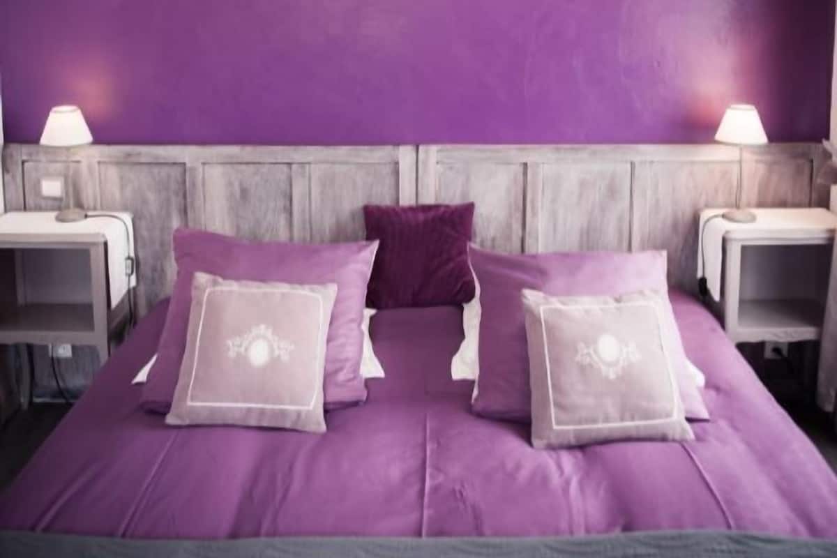 Un dormitorio con paredes moradas, un cabecero de madera y dos mesitas de noche con lámparas.