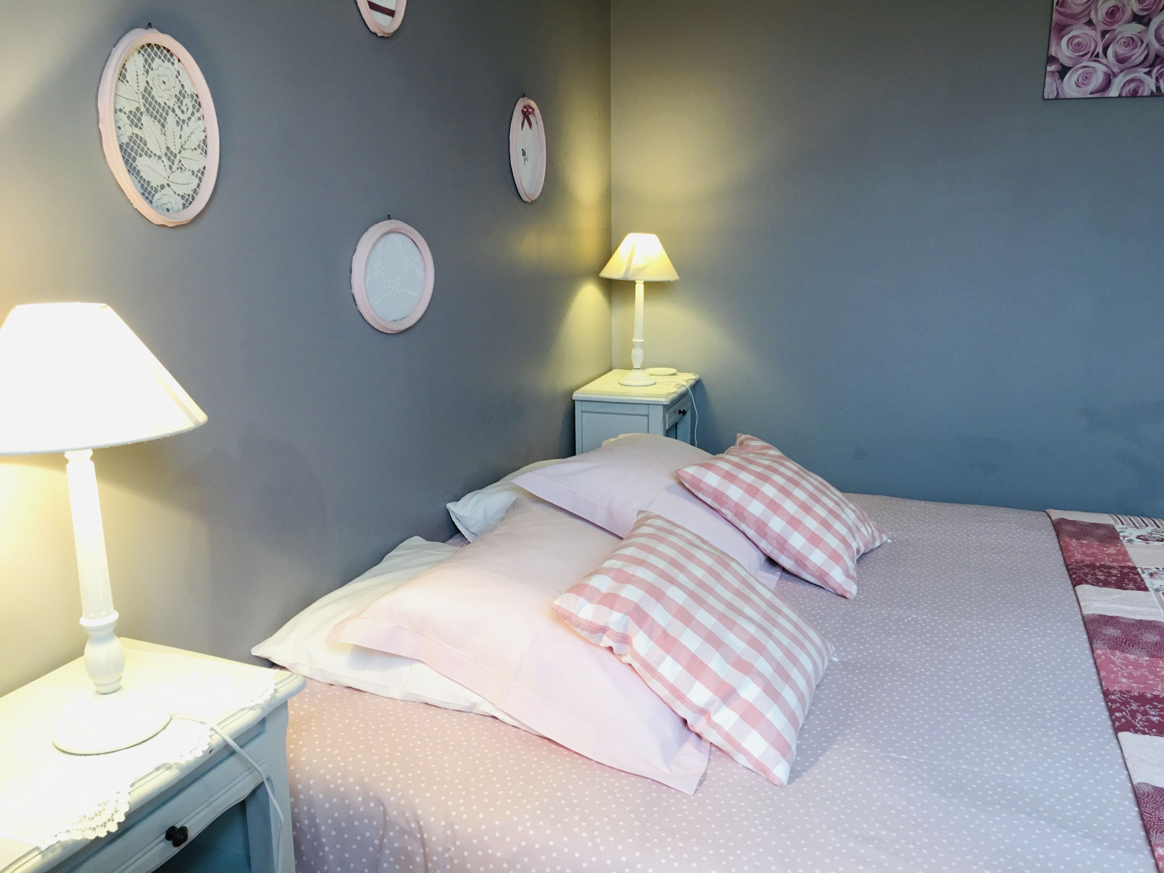 Een slaapkamer met een bed, kussens, een nachtkastje, een lamp en decoraties aan de muur.