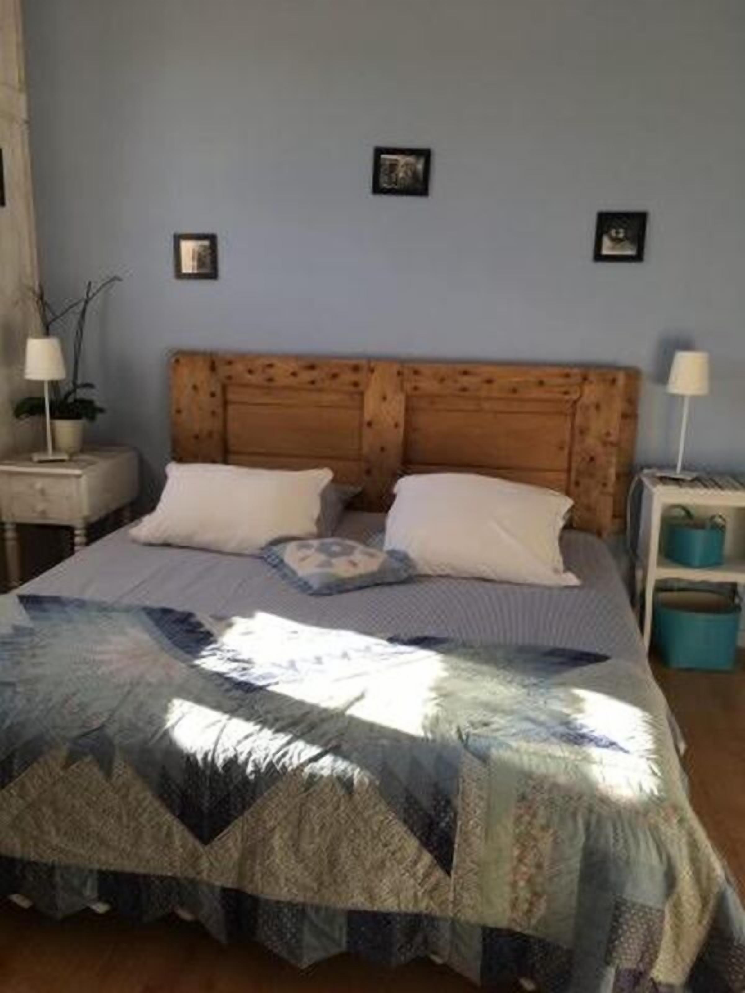 A bedroom with a wooden headboard, two white pillows, a quilted bedspread, and a nightstand with a lamp.