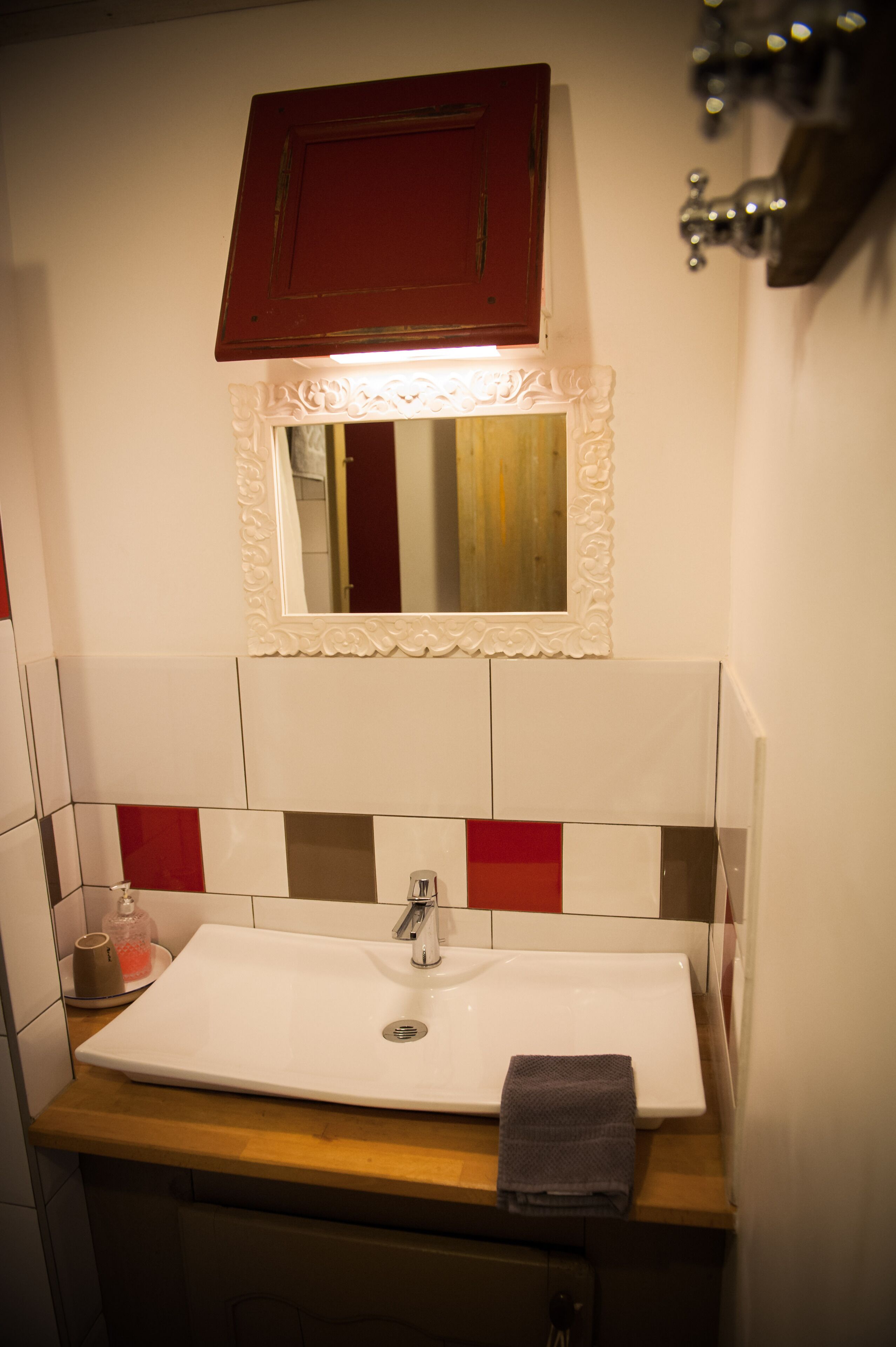 Un baño con un lavamanos blanco, baldosas rojo y blanco, una encimera de madera, un armario rojo y un espejo con un marco decorativo.