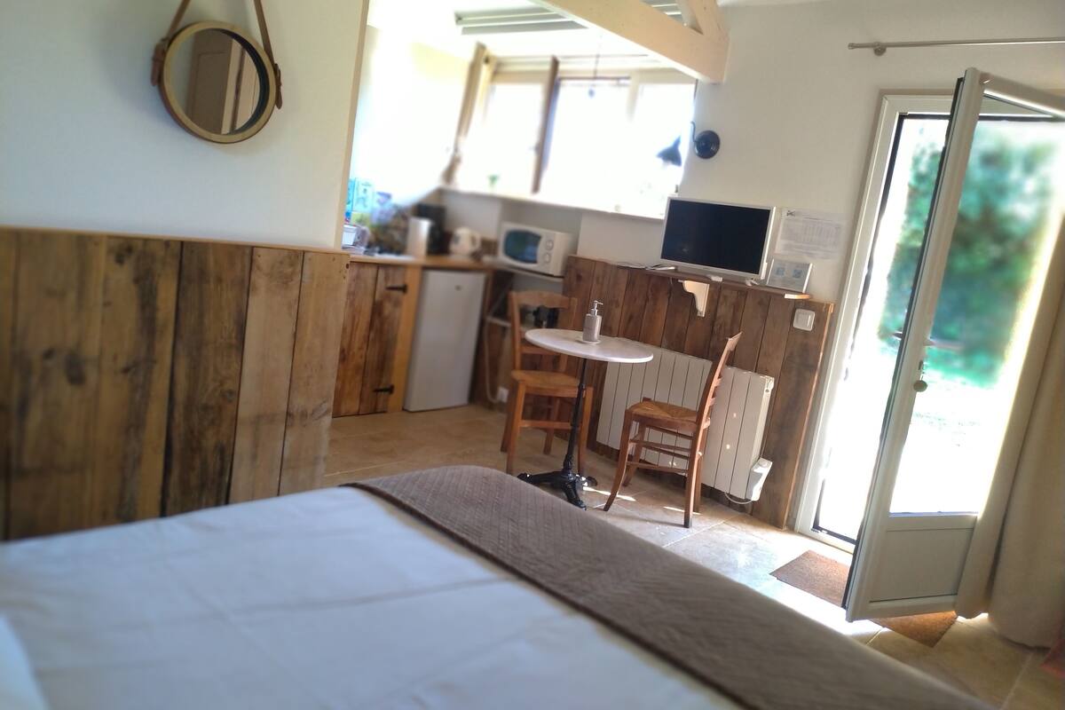Un dormitorio con cabecera de madera, una cama, una mesita con una silla y un televisor fijado a la pared.