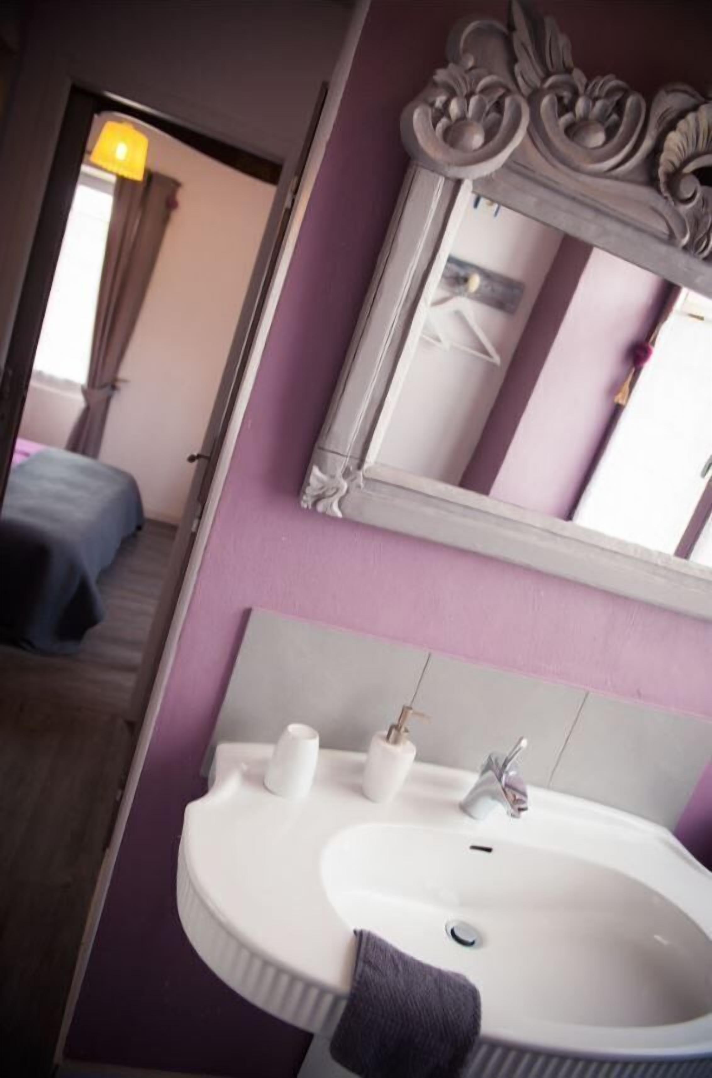 Ein Badezimmer mit einem weißen Waschbecken, einem Spiegel und einer violetten Wand.
