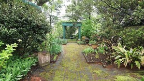 A garden pathway leading to a green archway surrounded by lush greenery and potted plants. - Double Oaks Bed and Breakfast (Greensboro)