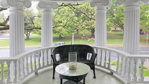 A covered porch with white columns, a glass table, and two wicker chairs. - Double Oaks Bed and Breakfast (Greensboro)
