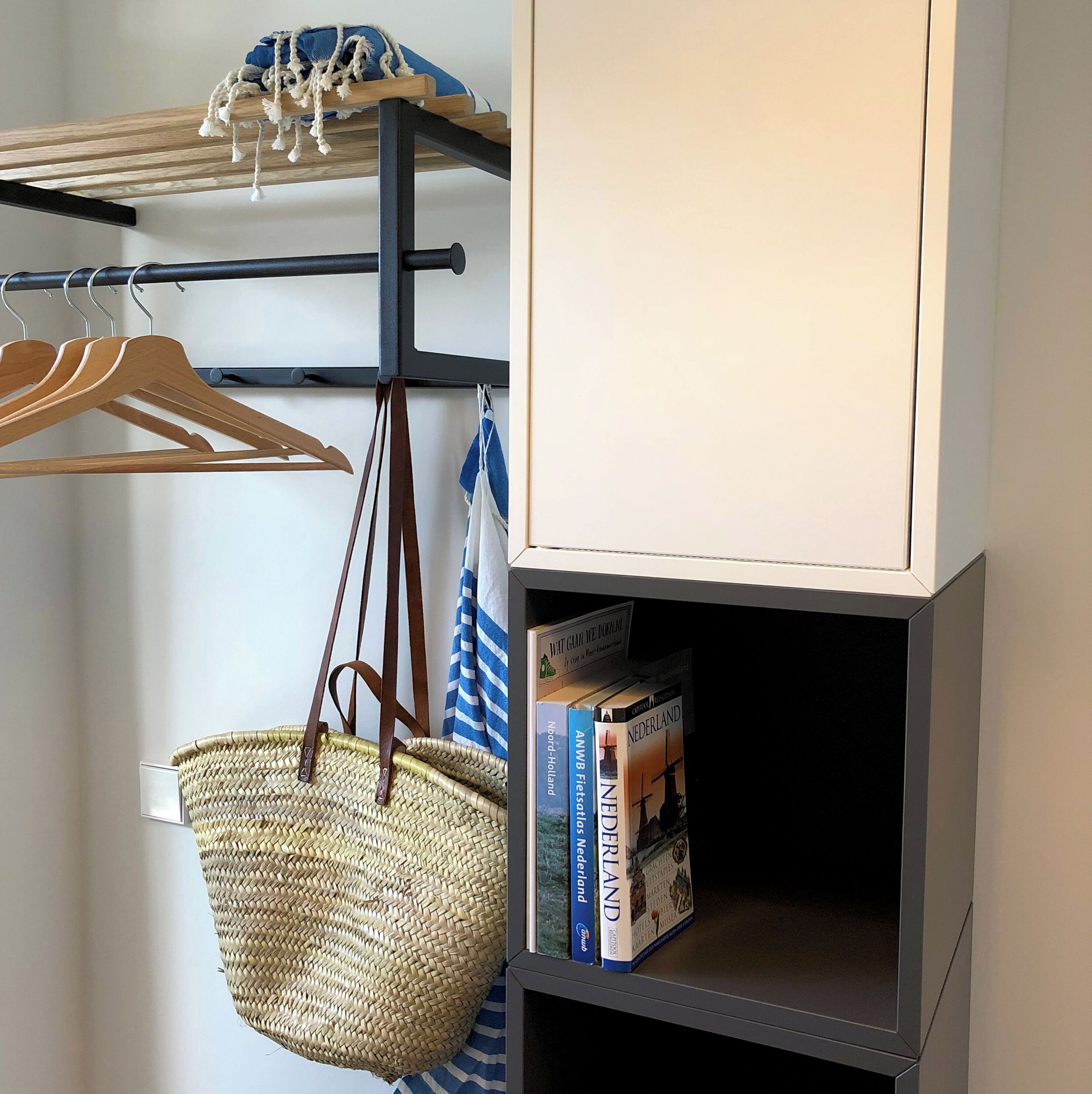 A room with a wooden drying rack, a wicker basket, and a bookshelf containing books and a sign.