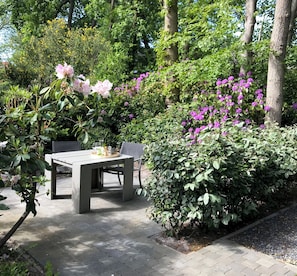 Relax in a serene garden setting with a table and chairs surrounded by lush greenery and vibrant flowers.