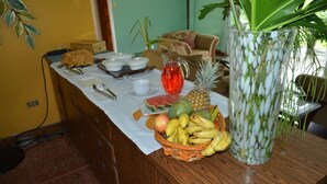 Une table avec un panier de fruits, une carafe et un vase rempli de fleurs blanches.
