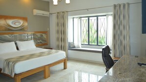 Une chambre d’hôtel avec un lit, un bureau, une chaise, une fenêtre avec des rideaux et un tableau au mur.