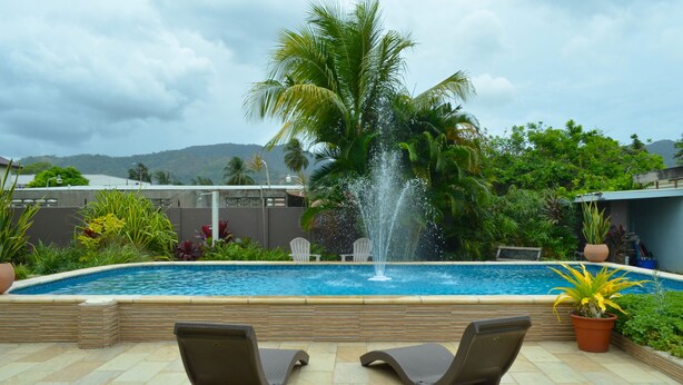 Une piscine agrémentée d’une fontaine, entourée de chaises longues et de plantes en pot.