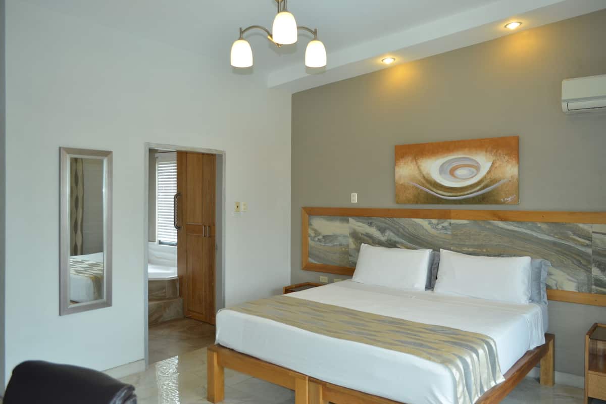 A bedroom with a bed, a wooden headboard, a painting on the wall, and a ceiling light fixture.