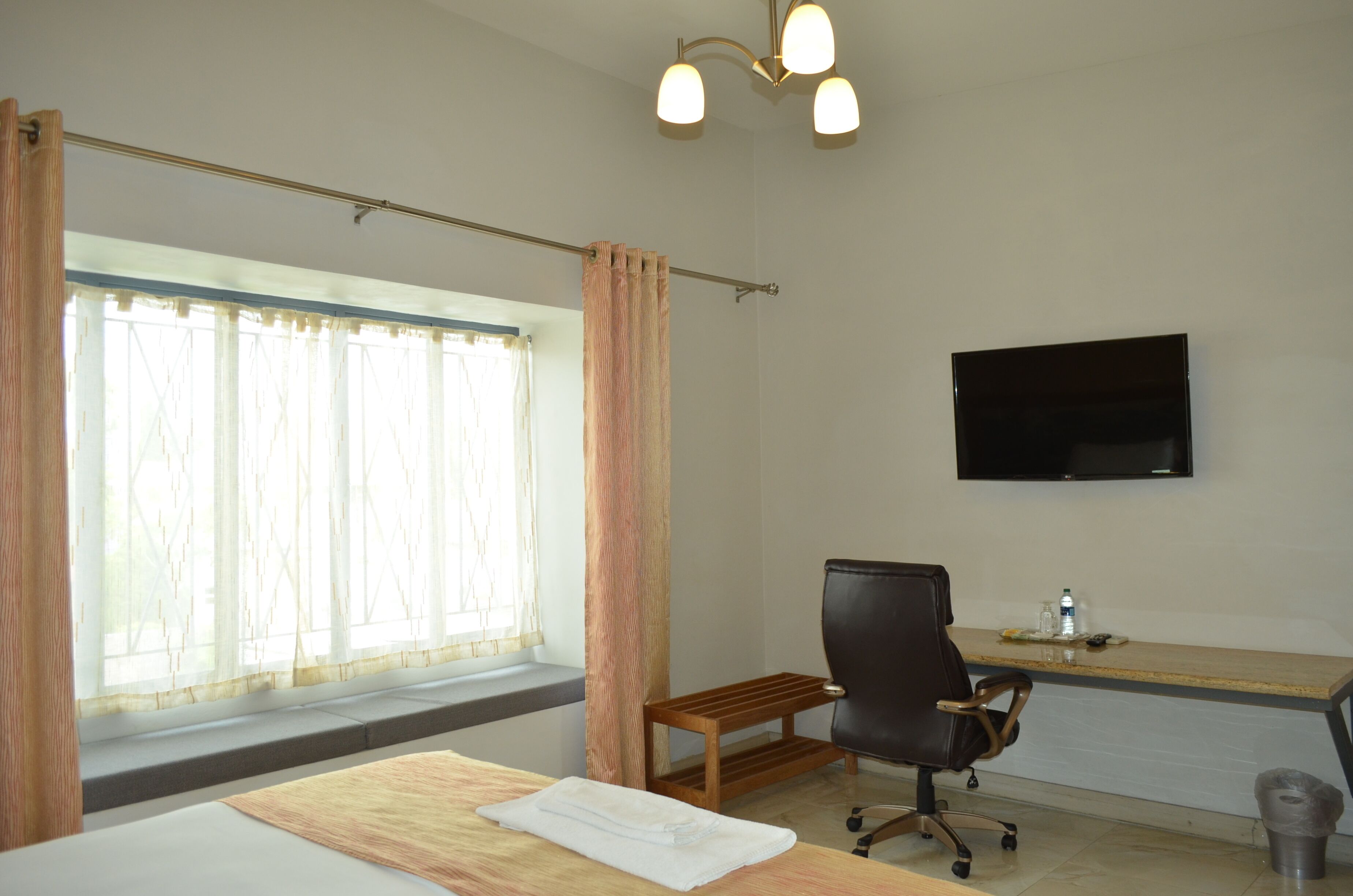 A hotel room with a bed, a desk, a chair, a TV, and a window with curtains.