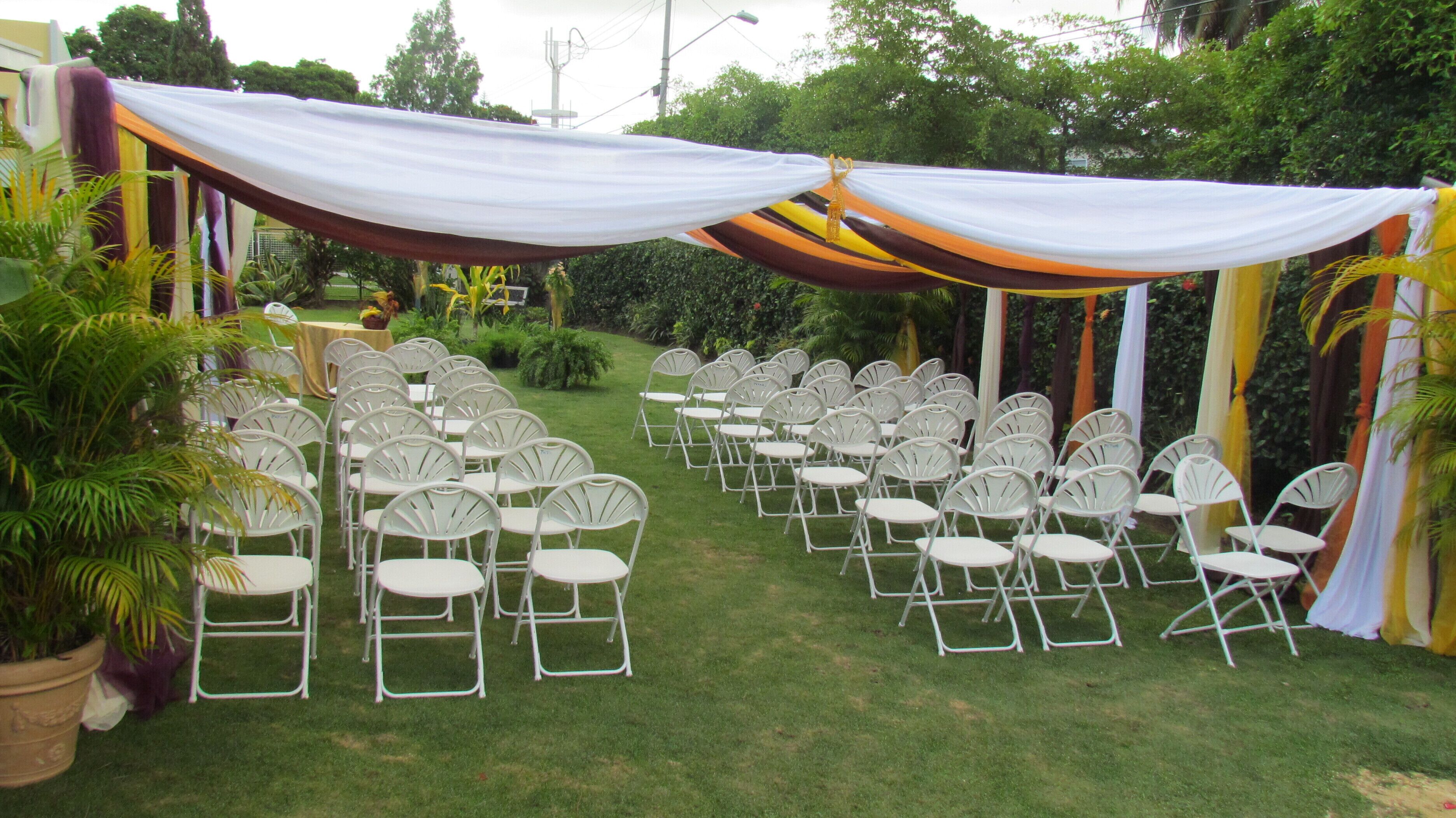 An outdoor event space with rows of white chairs and a draped canopy.