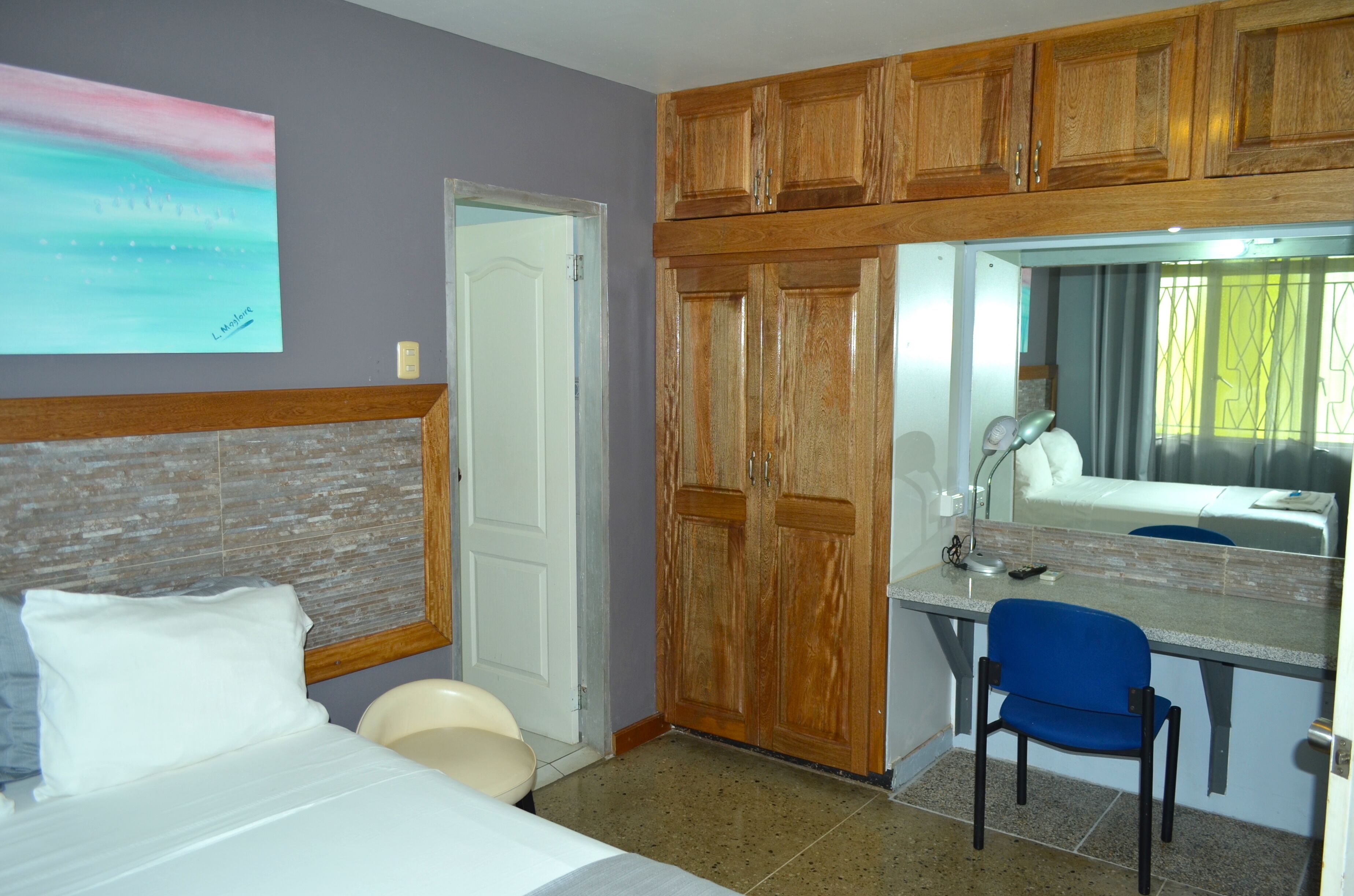 Ein Hotelzimmer mit einem Bett, einem Schreibtisch mit Stuhl, einem Holzschrank, einem Badezimmer und einem Bild an der Wand.