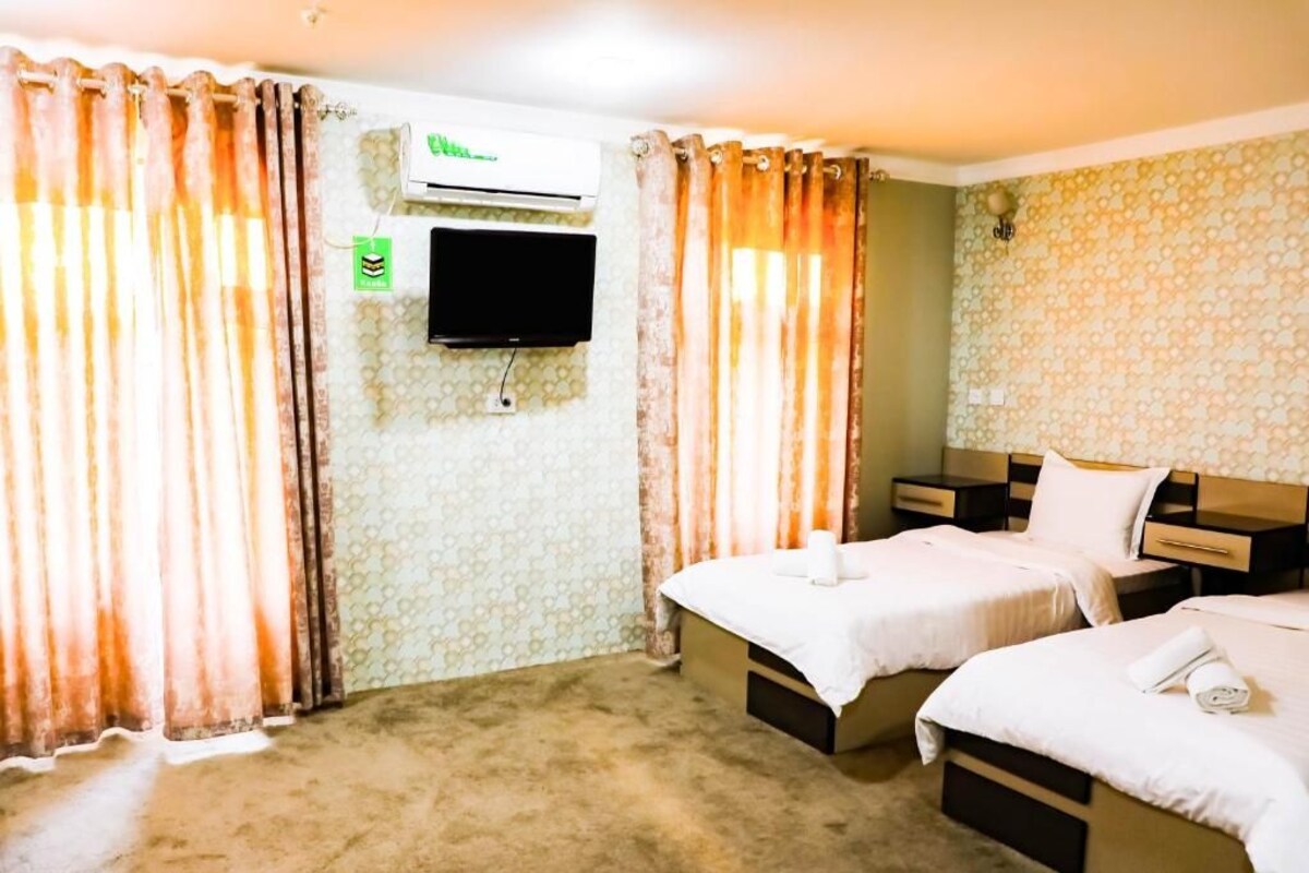A hotel room with two beds, a flat-screen TV mounted on the wall, and a patterned wallpaper.