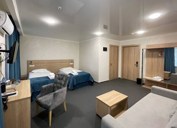A hotel room with two beds, a desk with a chair, a sofa, a small wooden table, and a mirror. -  Reikartz Kokand (Kokand)