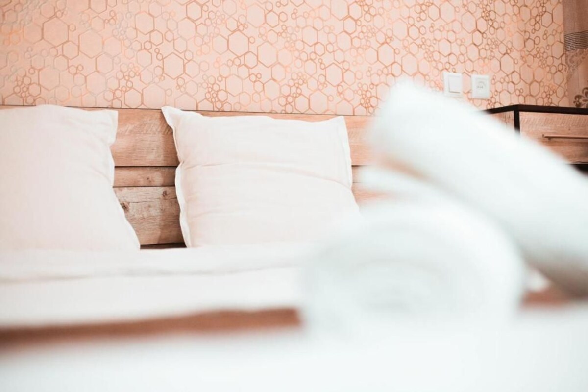 A bed with white bedding and a wooden headboard in a room with a honeycomb-patterned wall.