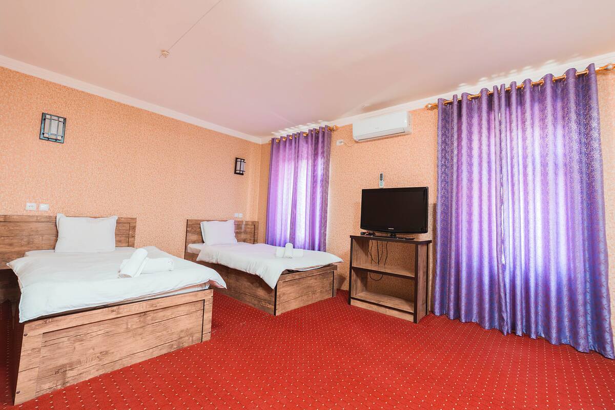 A hotel room with two wooden beds, a TV on a wooden stand, and purple curtains.