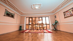 A spacious room with a large window, wooden flooring, and a dining area with chairs and a table. -  Reikartz Kokand (Kokand)