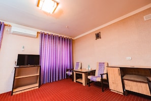 Habitación de hotel con televisor sobre un mueble, una mesita, dos sillas, un sofá y un equipo de aire acondicionado.