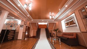 A spacious lobby with a central staircase, a reception desk, and a seating area. -  Reikartz Kokand (Kokand)