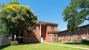 A two-story brick building with a central entrance, surrounded by a well-maintained lawn and trees. - 30-Night Minimum Studio Near Main Street (St Charles)